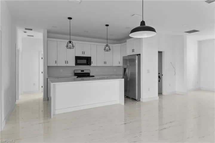 Kitchen with hanging light fixtures, stainless steel appliances, white cabinets, and a kitchen island