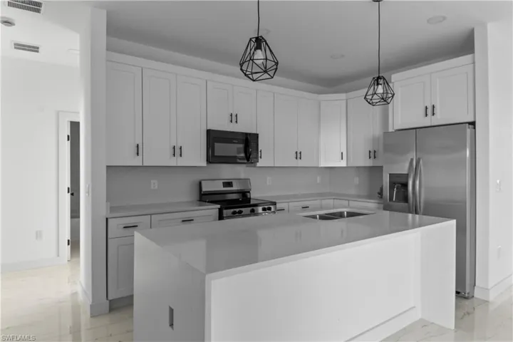 Kitchen with a center island, sink, hanging light fixtures, appliances with stainless steel finishes, and white cabinets