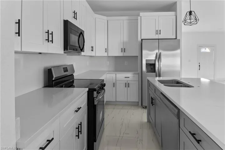 Kitchen with sink, hanging light fixtures, white cabinets, and stainless steel appliances