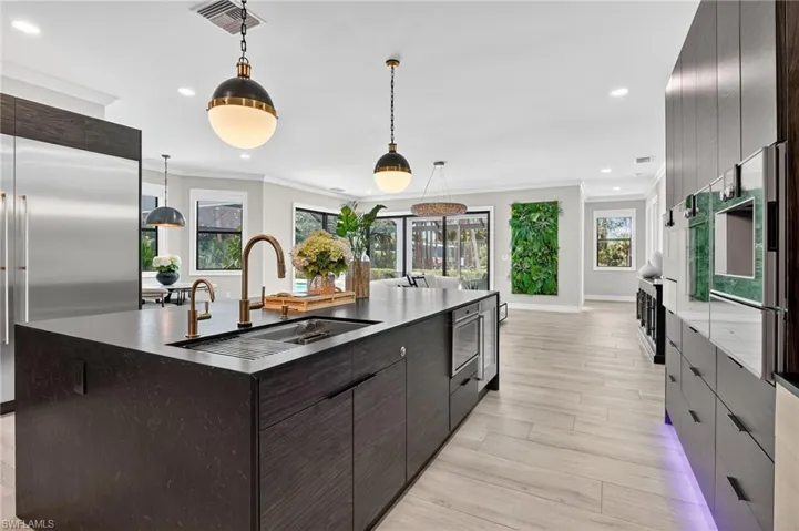 Kitchen with dark wood finish cabinets, modern cabinets, an island with sink, stainless steel appliances, and crown molding