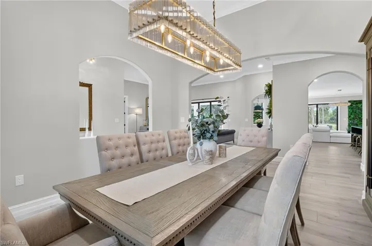 Dining area with ornamental molding, arched walkways, a high ceiling, light wood finished floors, and recessed lighting