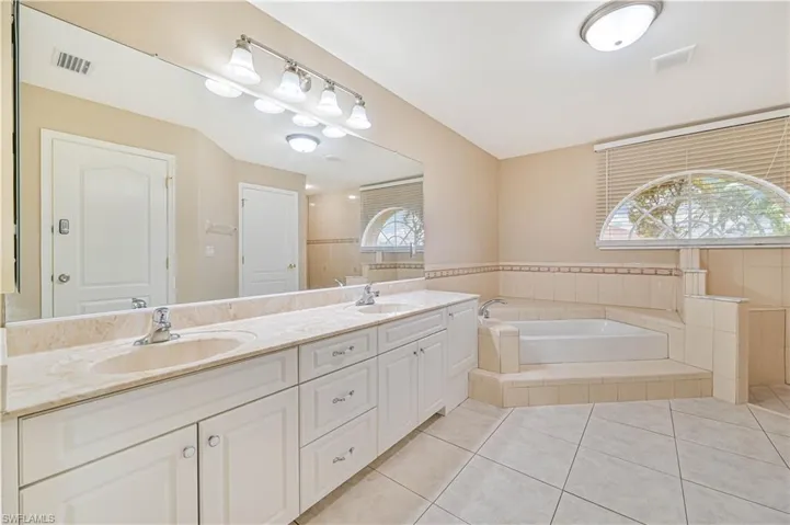Bathroom with tile patterned flooring, tiled bath, and dual bowl vanity
