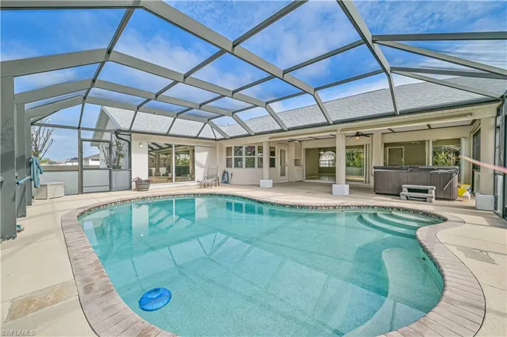View of pool with a hot tub, ceiling fan, and glass enclosure