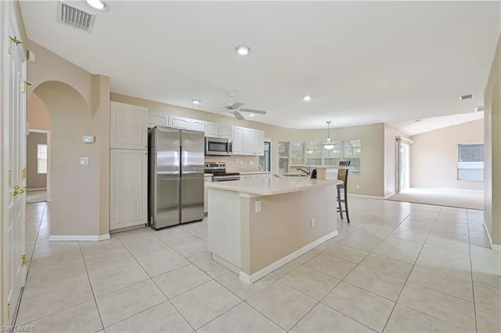 Kitchen with a kitchen island with sink, a kitchen bar, light tile patterned floors, and stainless steel appliances