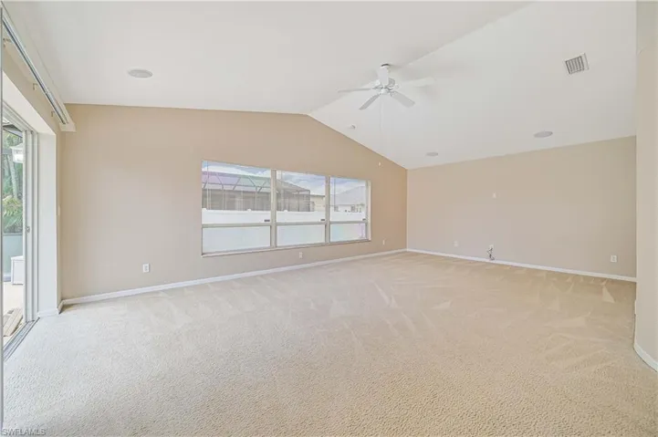 Unfurnished room featuring light carpet, a healthy amount of sunlight, ceiling fan, and vaulted ceiling