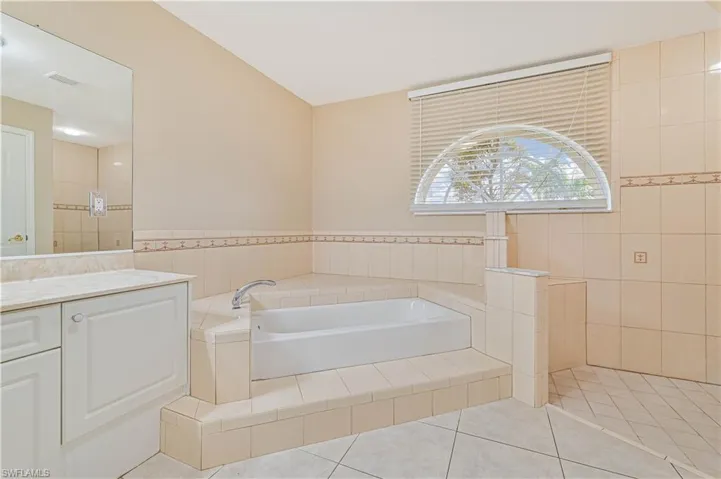 Bathroom with vanity, tile patterned flooring, tile walls, and a relaxing tiled tub
