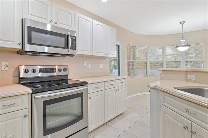 Kitchen with decorative light fixtures, white cabinets, light tile patterned floors, and stainless steel appliances