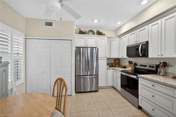 Kitchen featuring stainless steel appliances, white cabinetry, ceiling fan, light stone countertops, and light tile patterned flooring