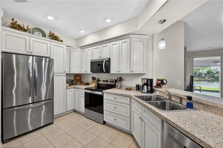 Kitchen featuring stainless steel appliances, light countertops, white cabinetry, and decorative light fixtures