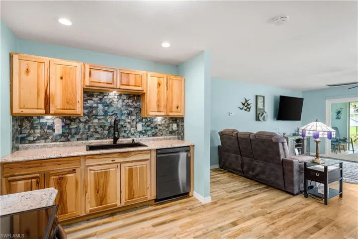 14937-Kitchen featuring dishwashing machine, sink, light stone countertops, and backsplash
