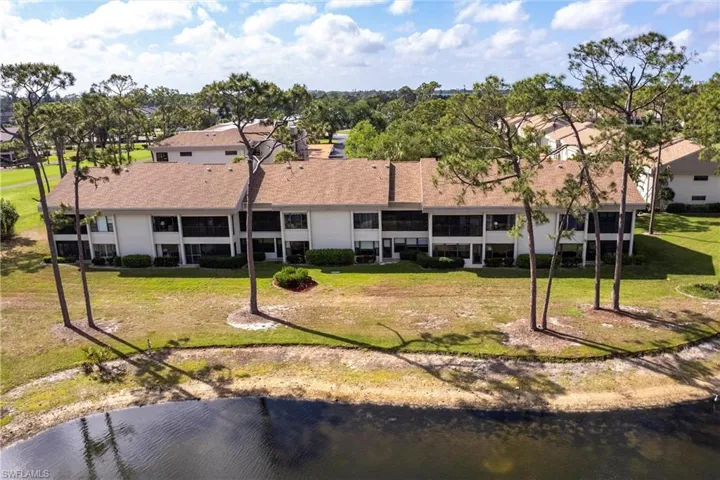 Rear view of property featuring stucco siding, a lawn, a water view, and a shingled roof