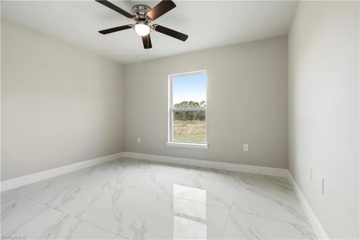 Spacious room featuring large format marble-look tile flooring, light neutral wall paint, and a ceiling fan with integrated lighting