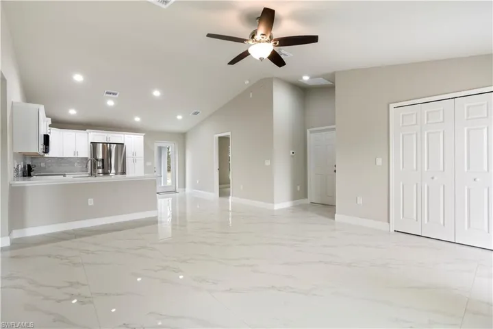Open concept living space featuring large format marble-look tile flooring, vaulted ceilings, recessed lighting, and a modern ceiling fan