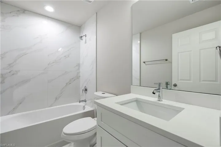 Bathroom featuring a rectangular undermount sink with a chrome faucet, a large vanity mirror, and a built-in tub with marble-look tile surround