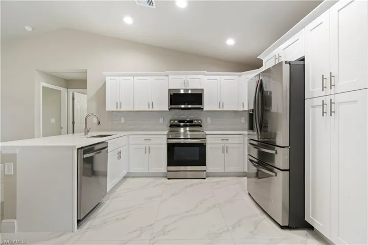 Modern kitchen featuring white shaker cabinetry, stainless steel appliances, a white quartz countertop, a gray subway tile backsplash, and white marble-look tile flooring