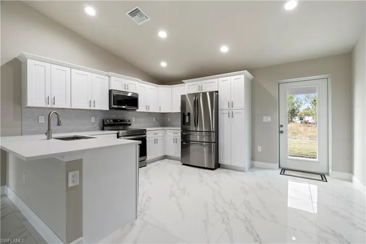 Modern kitchen featuring white shaker cabinetry, stainless steel appliances, a white quartz countertop island, and white marble-look tile flooring