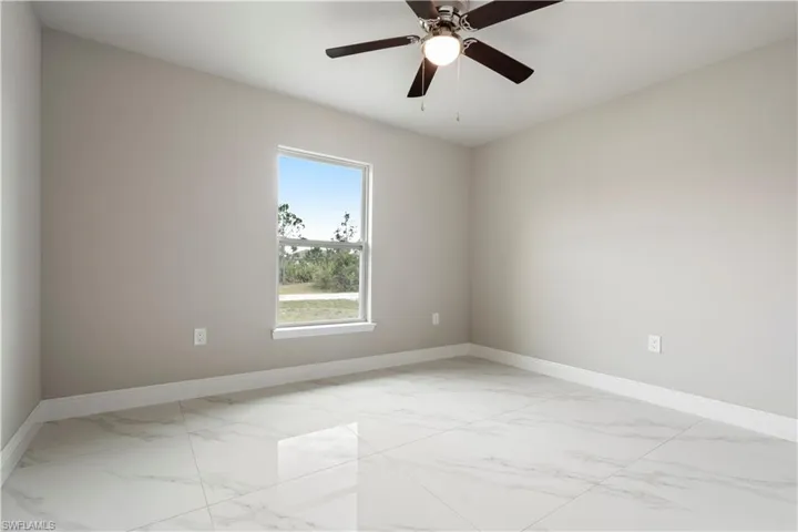 Spacious room featuring large format tile flooring, a single window, light neutral wall paint, and a ceiling fan with integrated lighting