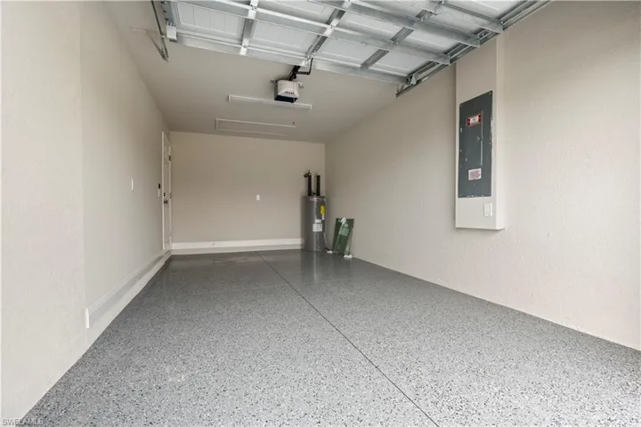Garage with speckled epoxy flooring, overhead garage door mechanism, wall-mounted electrical panel, interior access door, and a water heater