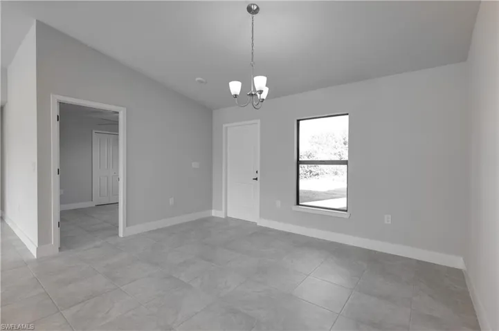 Tiled spare room featuring a chandelier and vaulted ceiling