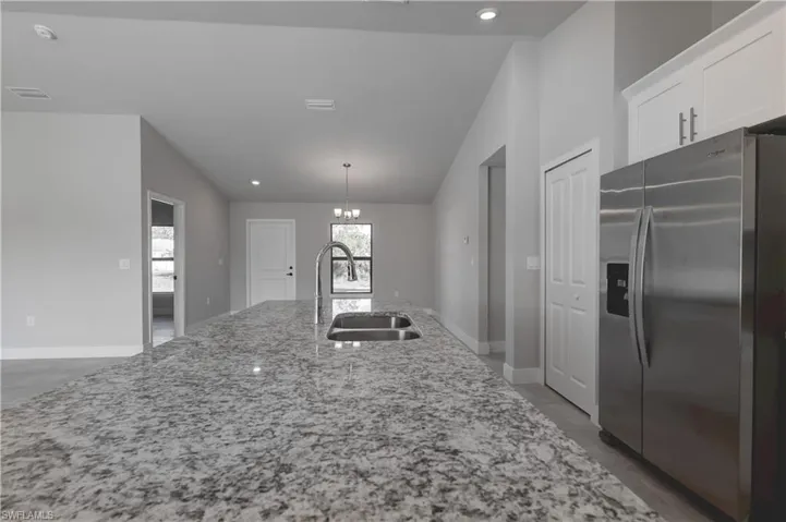 Kitchen with sink, light stone counters, decorative light fixtures, stainless steel refrigerator with ice dispenser, and white cabinetry