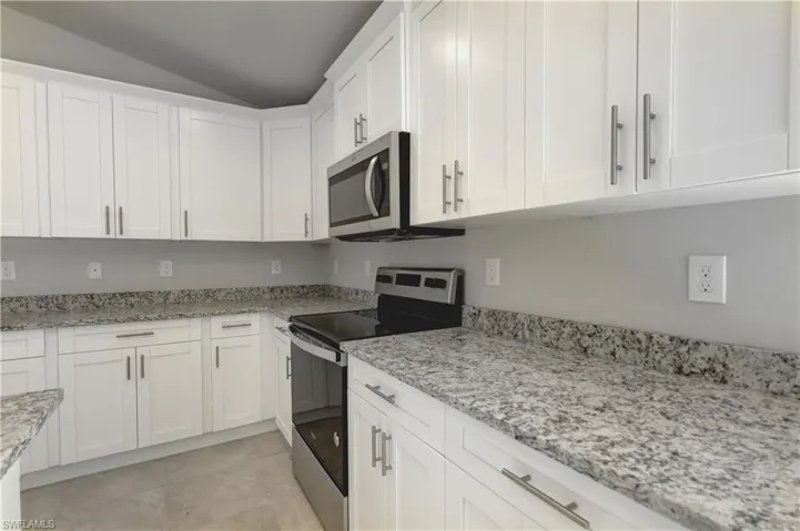 Kitchen featuring appliances with stainless steel finishes, white cabinets, light tile patterned floors, light stone countertops, and lofted ceiling