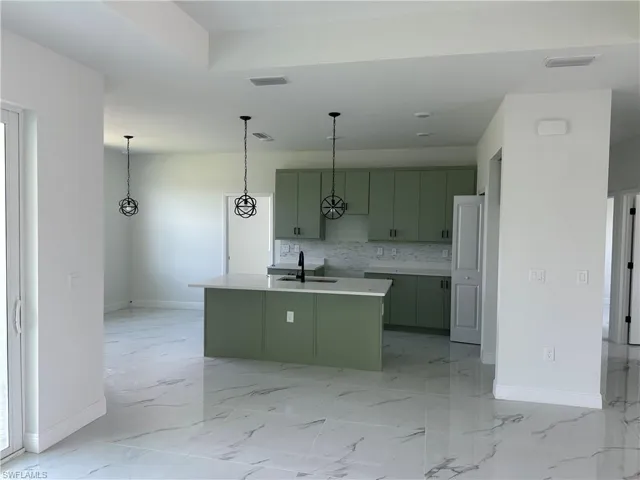 Kitchen featuring light tile patterned flooring, a center island with sink, green cabinetry, decorative backsplash, and sink