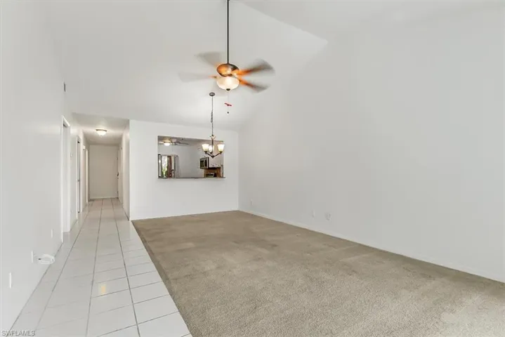 Unfurnished living room with light colored carpet, ceiling fan, light tile patterned flooring, and high vaulted ceiling