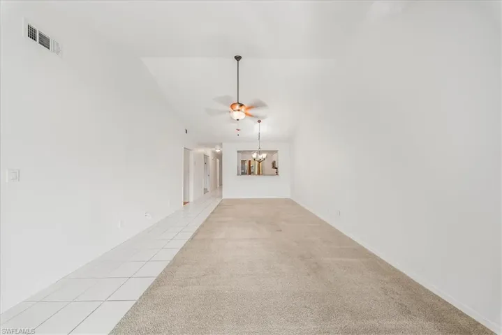 Carpeted spare room featuring tile patterned flooring, ceiling fan, a chandelier, and vaulted ceiling