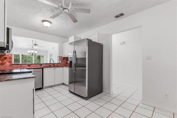 Kitchen with appliances with stainless steel finishes, a ceiling fan, dark stone countertops, light tile patterned floors, and a textured ceiling