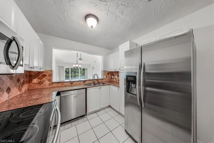Kitchen with appliances with stainless steel finishes, decorative backsplash, light tile patterned flooring, dark stone countertops, and a textured ceiling