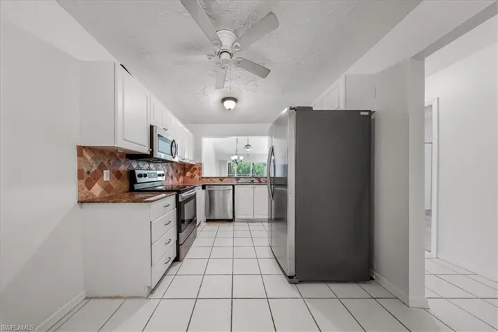 Kitchen with stainless steel appliances, light tile patterned floors, backsplash, white cabinets, and a ceiling fan