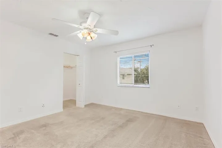 Unfurnished bedroom with light colored carpet, a spacious closet, and a ceiling fan