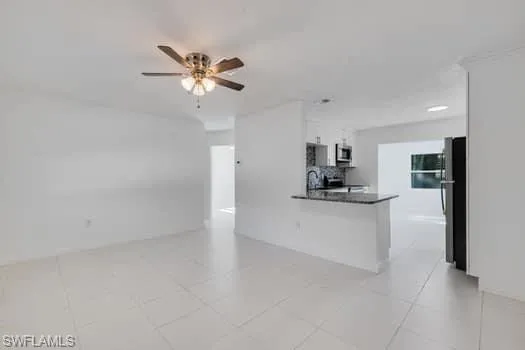 Kitchen with white cabinetry, a peninsula, freestanding refrigerator, a ceiling fan, and dark countertops