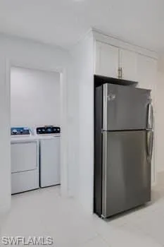 Kitchen with freestanding refrigerator, independent washer and dryer, white cabinetry, and light tile patterned floors