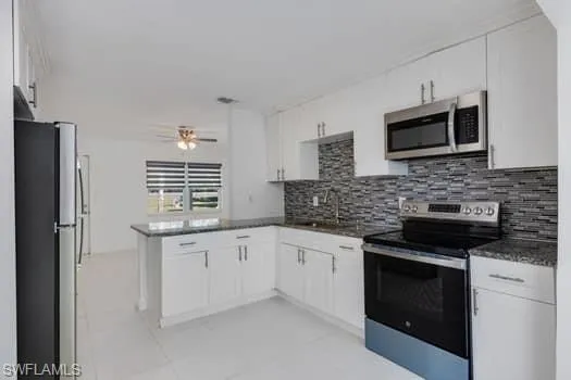 Kitchen with appliances with stainless steel finishes, white cabinets, decorative backsplash, and light tile patterned floors