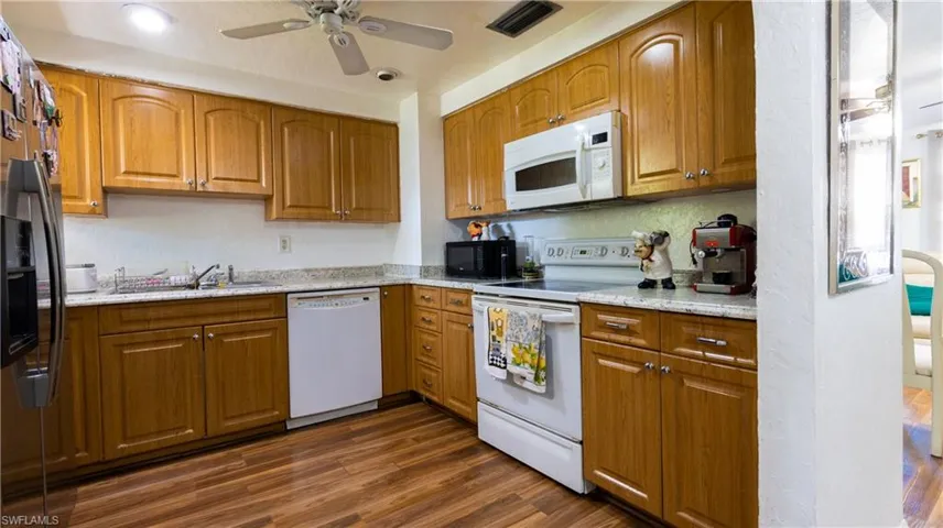 Kitchen with light stone countertops, dark wood-type flooring, white appliances, sink, and ceiling fan
