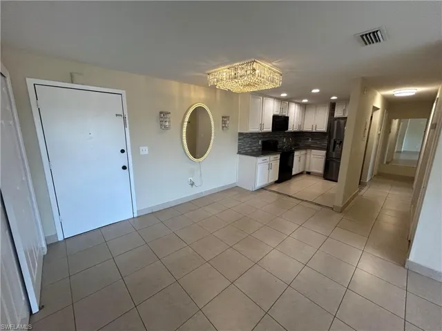 Kitchen with an inviting chandelier, tasteful backsplash, light tile patterned floors, black appliances, and white cabinets
