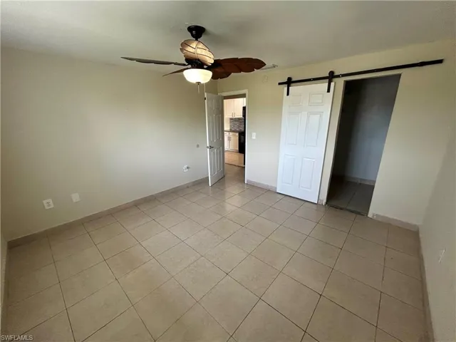 Unfurnished bedroom featuring ceiling fan, a barn door, and light tile patterned floors