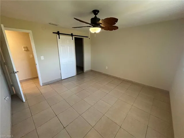 Unfurnished bedroom featuring ceiling fan, a barn door, and light tile patterned floors