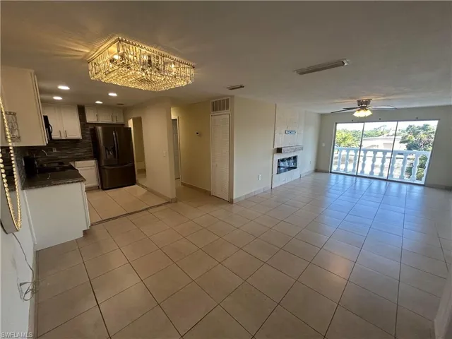 Kitchen featuring decorative backsplash, black fridge, ceiling fan with notable chandelier, white cabinets, and light tile patterned flooring