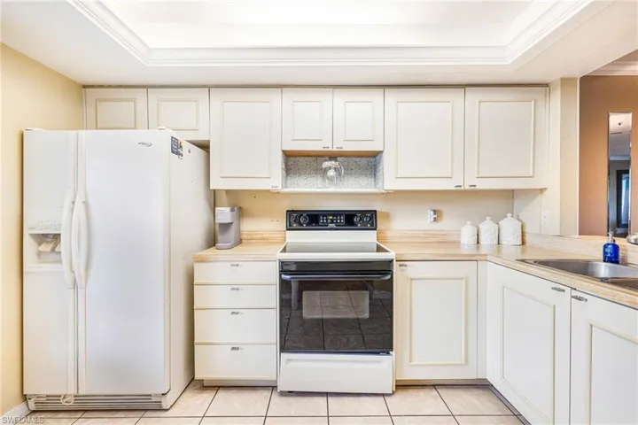 Kitchen featuring electric stove, white fridge with ice dispenser, light countertops, a raised ceiling, and light tile patterned flooring