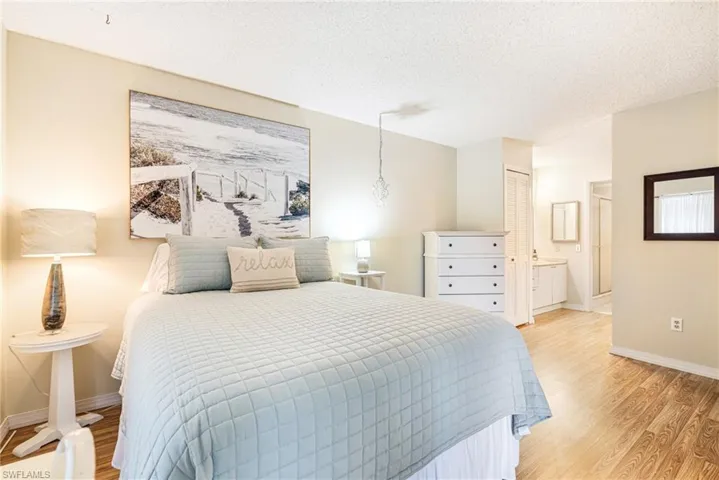 Bedroom with light wood finished floors, a textured ceiling, a closet, and ensuite bathroom