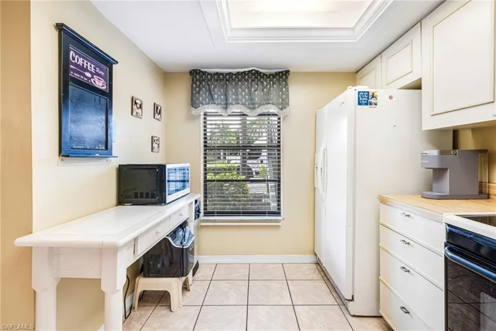 Kitchen with light countertops, white cabinets, black appliances, and light tile patterned floors