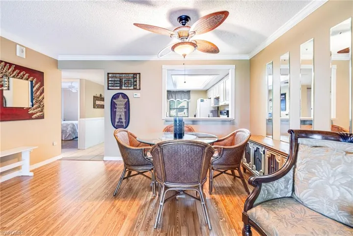 Dining space with a textured ceiling, light wood-type flooring, crown molding, and ceiling fan