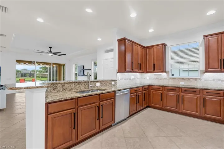 Kitchen featuring decorative backsplash, light stone counters, kitchen peninsula, dishwasher, and sink
