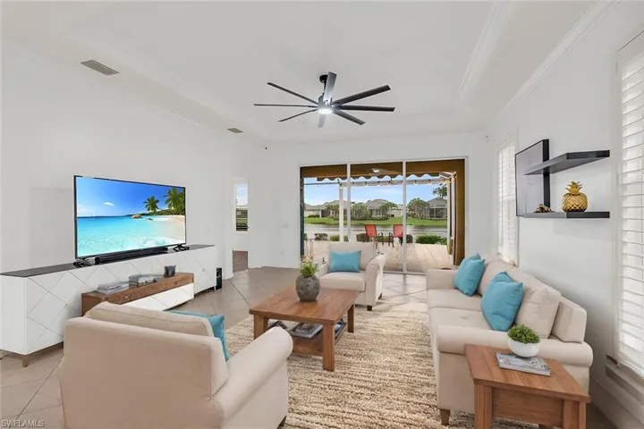 Tiled living room featuring ceiling fan, a raised ceiling, and crown molding