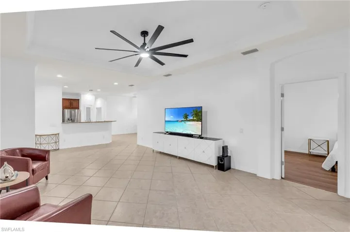 Tiled living room featuring ceiling fan, a tray ceiling, and ornamental molding
