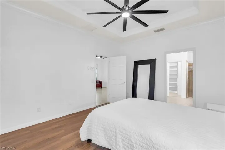 Bedroom with hardwood / wood-style flooring, a raised ceiling, crown molding, a spacious closet, and ceiling fan