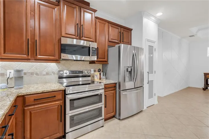Kitchen featuring light tile patterned flooring, backsplash, light stone countertops, stainless steel appliances, and ornamental molding