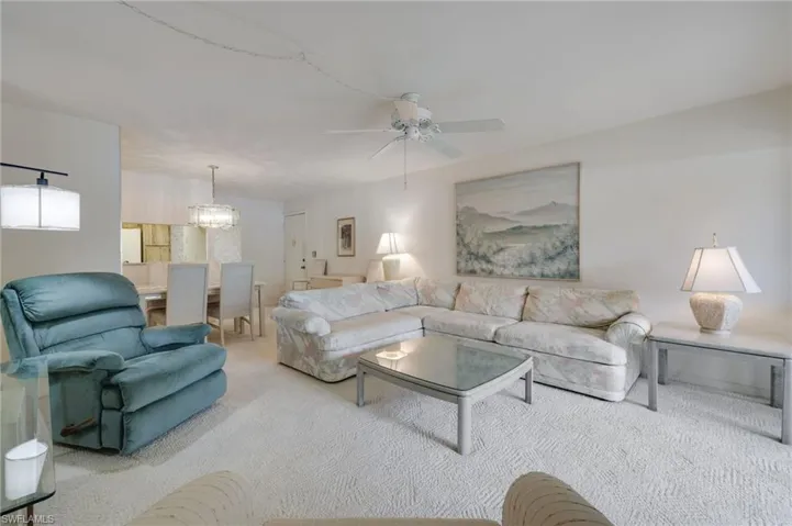 Living room with ceiling fan with notable chandelier and carpet flooring